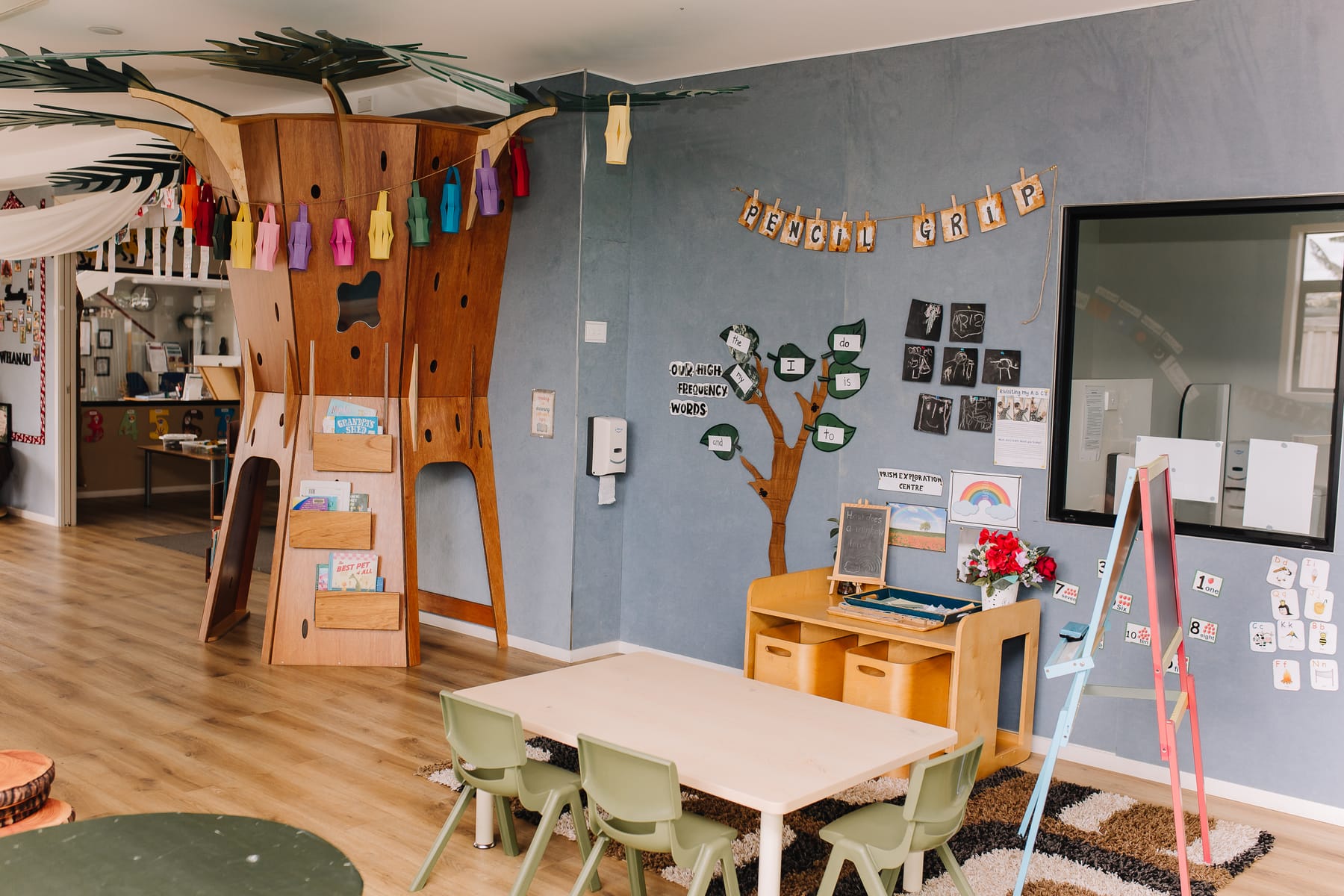 An indoor climbing and reading structure built to look like a tree, beside low tables and chairs.