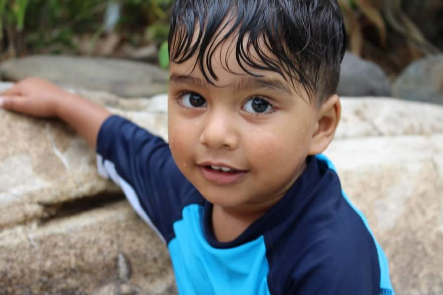 A child in a blue rash top leaning on a rock, hair still wet from the water.