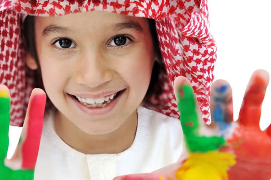 A smiling child holding both palms up to the camera, covered in bright finger paint.