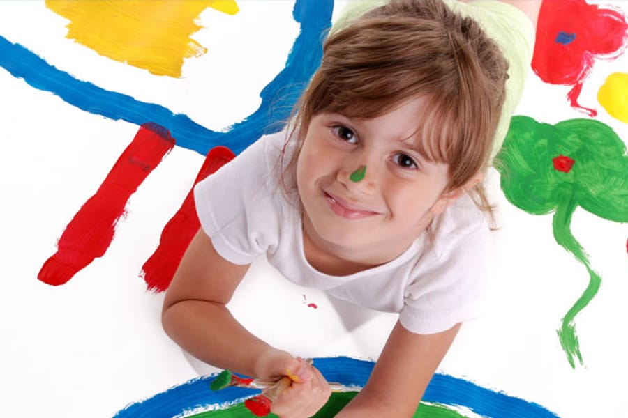 A child lying on a large sheet of paper covered in painted flowers and handprints.